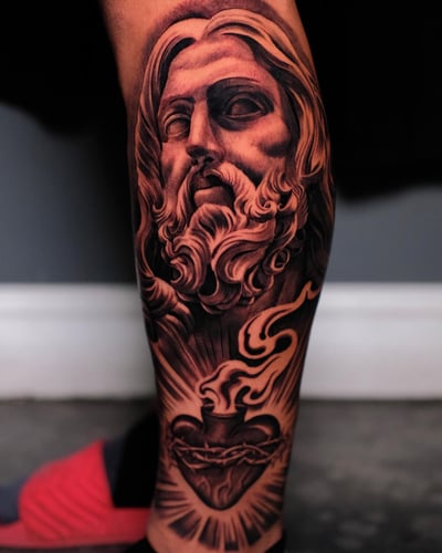 A detailed black and grey tattoo of Jesus Christ with a Sacred Heart on the calf, featuring realistic shading and spiritual symbolism — by Johnny Ayala, los angeles