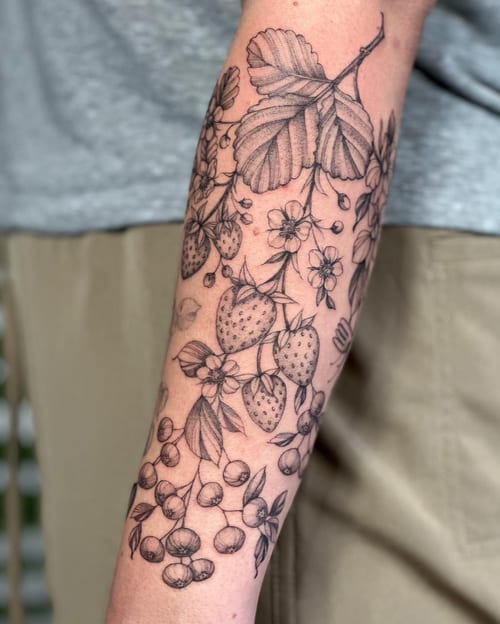 A delicate black and grey tattoo of a strawberry plant with flowers on the forearm, featuring fine line botanical details — by Melanie Benoit, los angeles