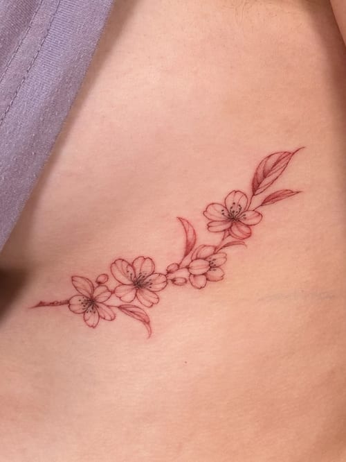 A delicate fine line cherry blossom branch tattoo on the rib, featuring minimal color and a minimalist style — by Melanie Benoit, los angeles