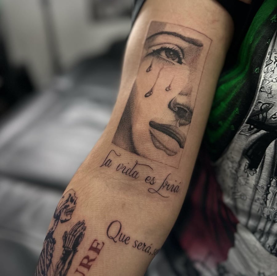 A black and grey Virgin Mary's face with tears and script on the upper arm, done in blackwork style — by Maddie Ramirez, los angeles