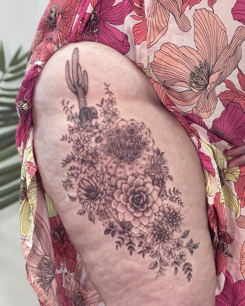 A detailed black and grey tattoo of a cactus and floral arrangement on the thigh, featuring intricate flower designs — by Melanie Benoit, los angeles