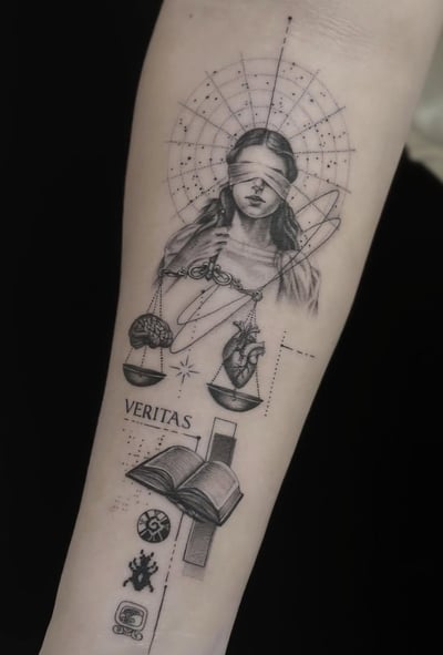 A black and grey fine line tattoo on the forearm depicting a blindfolded woman holding scales with a heart and brain, accompanied by the word 'VERITAS' and various symbolic elements — by Jian Liang…