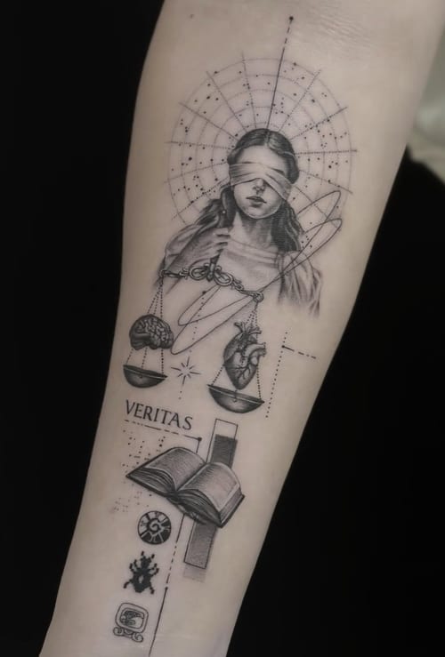 A black and grey fine line tattoo on the forearm depicting a blindfolded woman holding scales with a heart and brain, accompanied by the word 'VERITAS' and various symbolic elements — by Jian Liang…