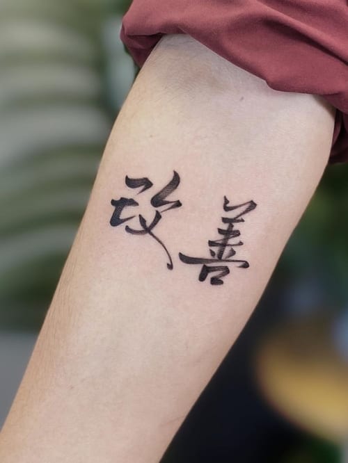 A black and grey lettering tattoo on the forearm featuring stylized script characters — by Jian Liang, los angeles