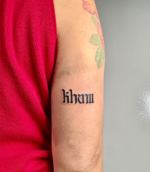 A bold black script lettering tattoo on the arm in a blackwork style — by Brian Kies, los angeles