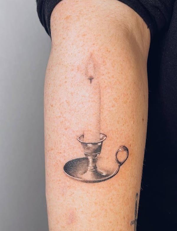 A black and grey realism tattoo of a candle on a holder, placed on the upper arm with fine shading and detail — by Level tattoo, los angeles