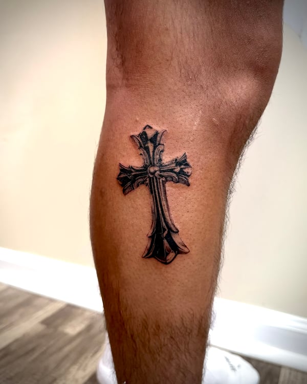 A black and grey tattoo of a stylized cross on the calf, featuring bold lines and shading — by emily, rahway