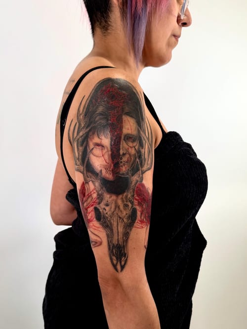 A mixed color and black and grey tattoo on the upper arm featuring a woman's face intertwined with a skull, showcasing a dark and realistic style — by zitronxus, los angeles