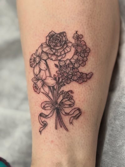 A delicate fine line black and grey bouquet of flowers tattoo on the leg, featuring roses and other floral elements — by Sandra Price, los angeles