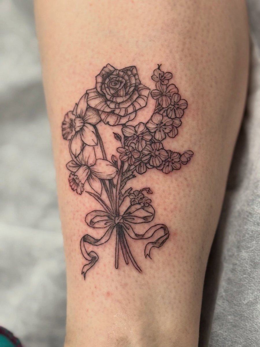 A delicate fine line black and grey bouquet of flowers tattoo on the leg, featuring roses and other floral elements — by Sandra Price, los angeles