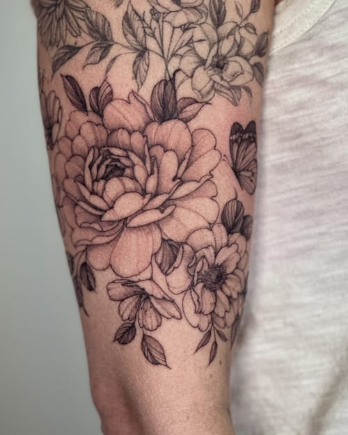A delicate black and grey floral bouquet with a butterfly on the arm, featuring detailed linework and shading — by Melanie Benoit, los angeles
