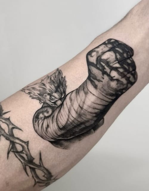 A black and grey anime-style tattoo of Garou with a dynamic pose on the forearm, featuring bold lines and shading — by otaybeatdown, los angeles