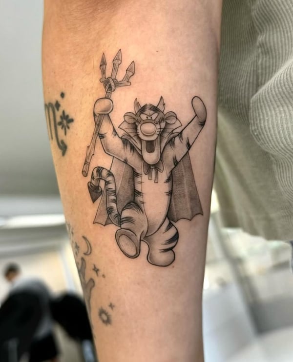 A black and grey linework tattoo of a cartoon tiger holding a trident, located on the calf with bold outlines and playful expression — by otaybeatdown, orange, ca