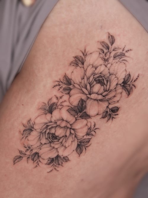 A delicate black and grey floral bouquet tattoo on the thigh, featuring fine line details and soft shading — by Melanie Benoit, los angeles