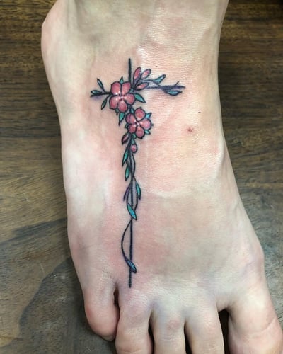 A delicate floral cross tattoo on the foot with fine line work and colorful flowers — by Sandra Price, los angeles