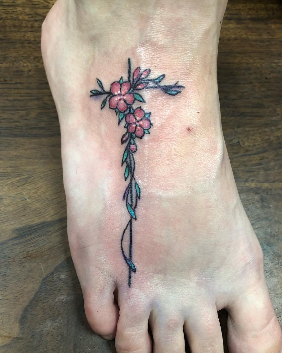 A delicate floral cross tattoo on the foot with fine line work and colorful flowers — by Sandra Price, los angeles