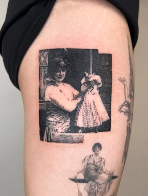 A black and grey realism tattoo of a vintage photograph depicting a woman holding a baby, located on the thigh with detailed shading — by Level tattoo, los angeles