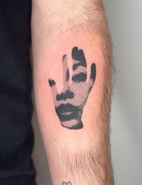 An abstract blackwork tattoo on the forearm depicting a hand with a face integrated into the design using striped patterns — by Level tattoo, los angeles