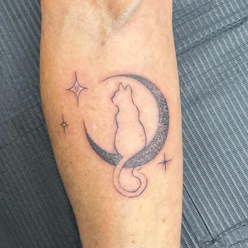 A minimalist black and grey tattoo of a cat sitting on a crescent moon with dotwork shading on the forearm — by Sandra Price, los angeles