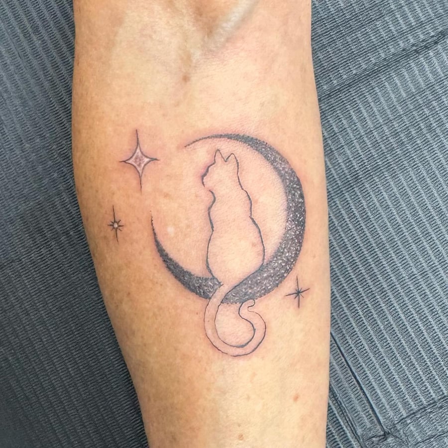 A minimalist black and grey tattoo of a cat sitting on a crescent moon with dotwork shading on the forearm — by Sandra Price, los angeles