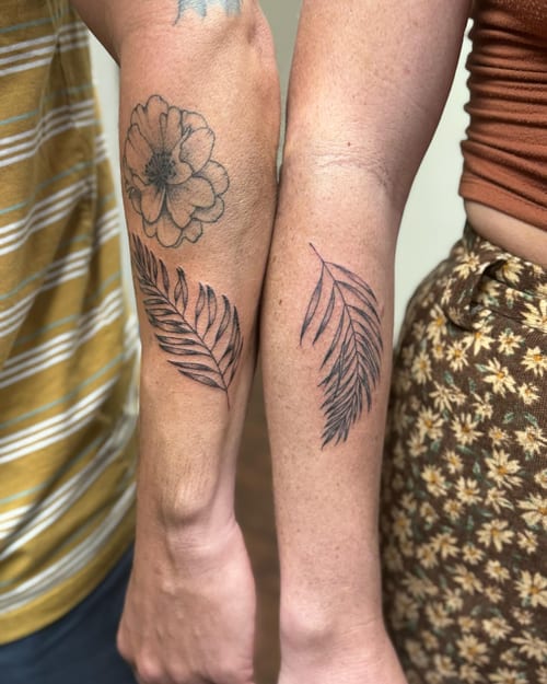 A delicate black and grey tattoo of a flower and leaves on the forearm, done in a fine line minimalist style — by Sandra Price, los angeles