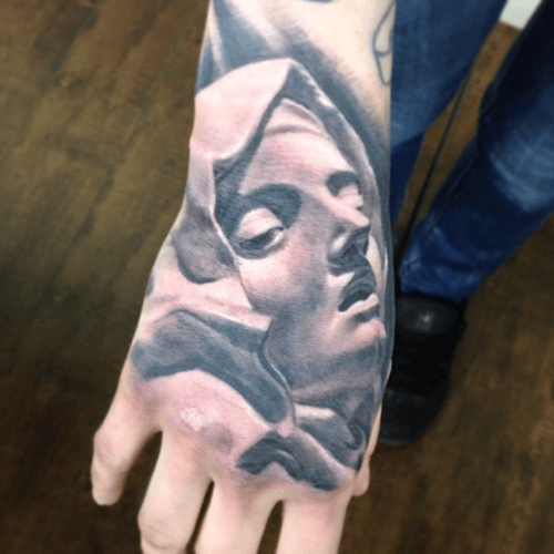 A black and grey realism tattoo of a serene face on the hand, featuring detailed shading and lifelike features — by tyler_whitlock, los angeles