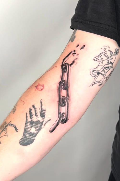 An illustrative black and grey tattoo on the forearm featuring a hand reaching towards a chain, with dotwork details — by Level tattoo, los angeles