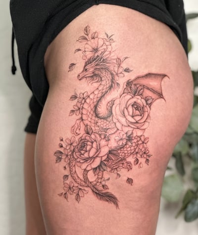A delicate black and grey dragon entwined with flowers on the thigh, featuring intricate detailing and ornate design — by Melanie Benoit, los angeles