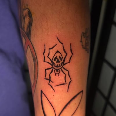 A bold blackwork tattoo of a skull spider on the forearm, featuring minimalist linework — by Miguel ANGELO, los angeles