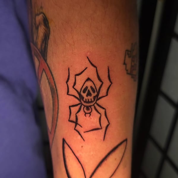 A bold blackwork tattoo of a skull spider on the forearm, featuring minimalist linework — by Miguel ANGELO, temecula, ca