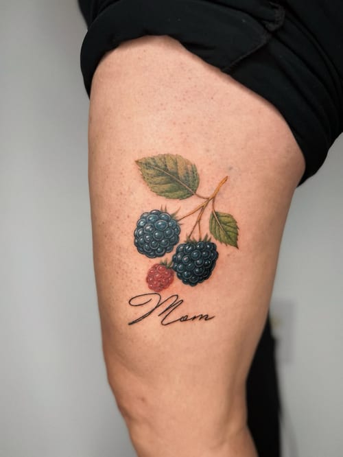 A realistic color tattoo of blackberries with the word 'Mom' in script on the thigh — by lunayflorestattoo, los angeles
