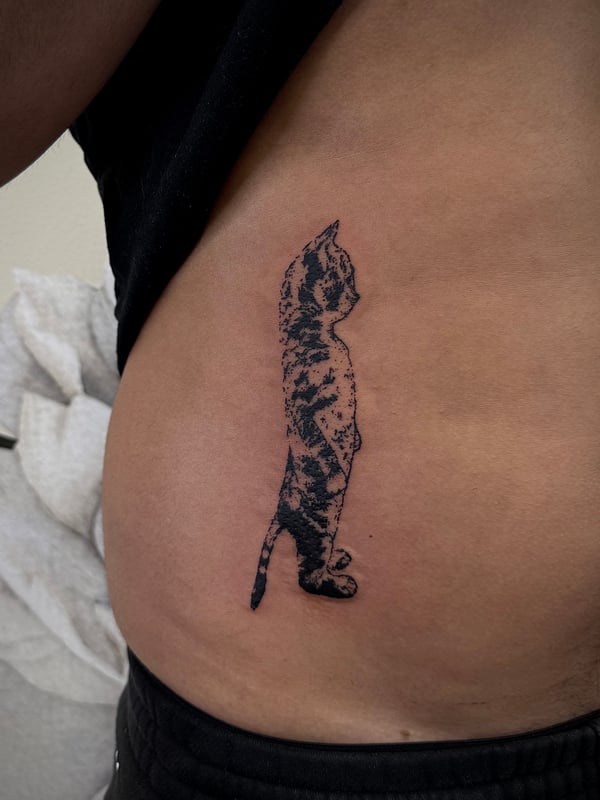 A minimalist blackwork tattoo of a standing cat silhouette on the rib, featuring a textured pattern within the outline — by emily, rahway