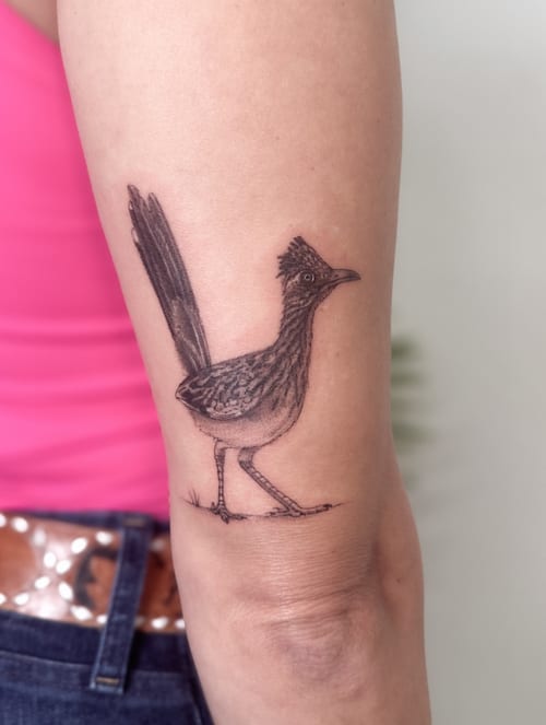 A realistic black and grey roadrunner tattoo on the arm, showcasing detailed feather texture and clean lines — by Melanie Benoit, los angeles