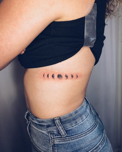A minimalist black and grey moon phase tattoo on the rib, featuring delicate celestial imagery — by Level tattoo, los angeles