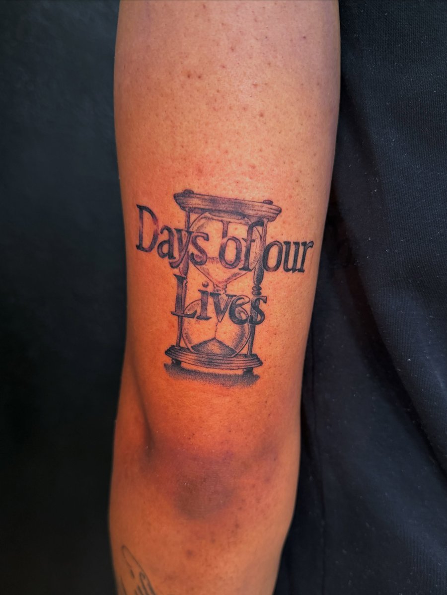A black and grey hourglass with the text 'Days of our Lives' on the forearm, featuring bold script lettering — by Kiera Garvin, los angeles