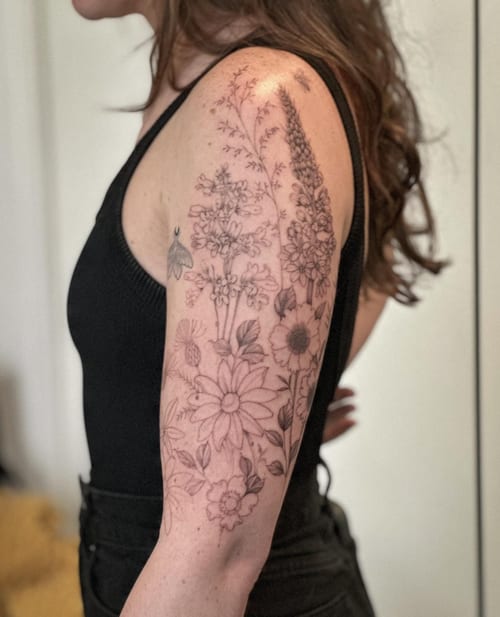 A delicate black and grey floral arrangement tattoo on the upper arm with fine line details — by Melanie Benoit, los angeles