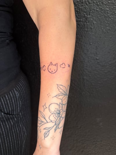 A minimalist linework tattoo of a cat face with hearts on the forearm, featuring a simple and whimsical design — by Kiera Garvin, los angeles