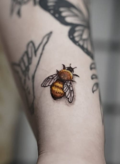 A realistic color tattoo of a bee on the forearm, featuring fine line details and vibrant yellow and black hues — by Shelby Bianco, los angeles
