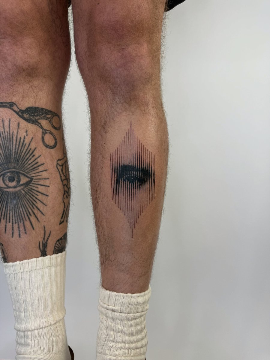 A bold black and grey eye tattoo with geometric linework on the calf, featuring a graphic style — by Level tattoo, los angeles