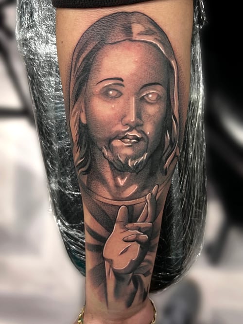 A realistic black and grey portrait of a religious figure on the forearm, showcasing detailed shading and lifelike features — by Josue Bravo, los angeles