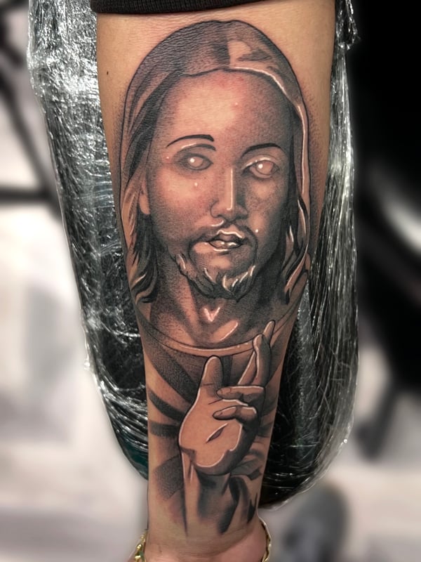 A realistic black and grey portrait of a religious figure on the forearm, showcasing detailed shading and lifelike features — by Josue Bravo, los angeles