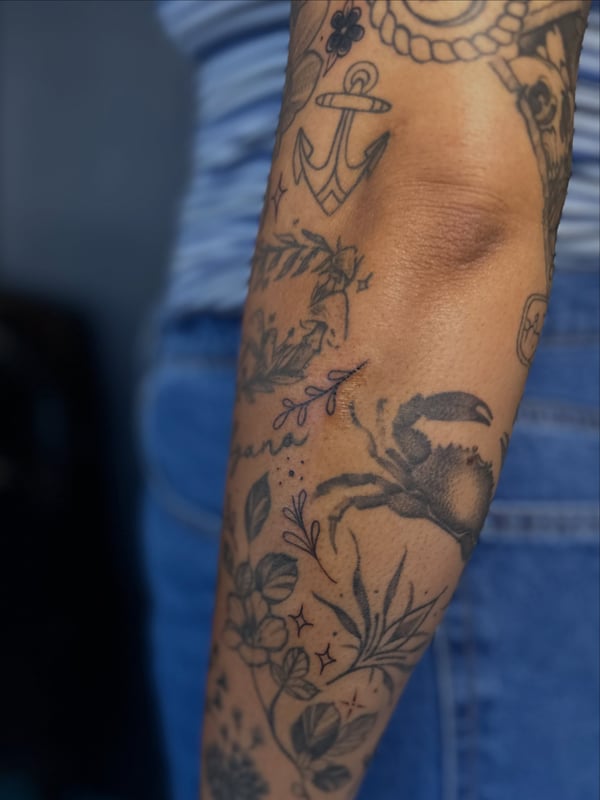 A black and grey floral and anchor filler tattoo on the forearm in an illustrative style — by Maddie Ramirez, palm desert, ca