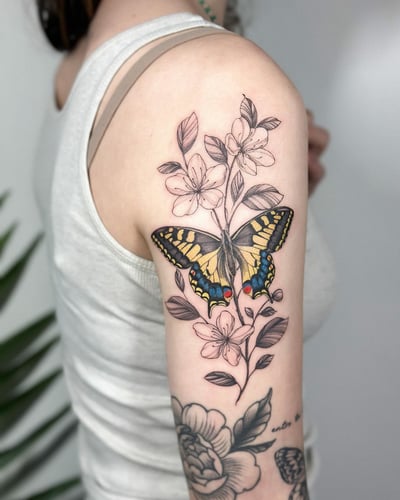 A colorful butterfly and blackwork floral tattoo on the upper arm, combining neo-traditional and delicate styles — by Melanie Benoit, los angeles