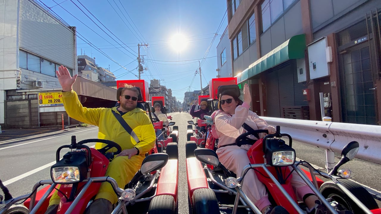 Adam and Lindsay driving go karts past shops and buildings in Tokyo