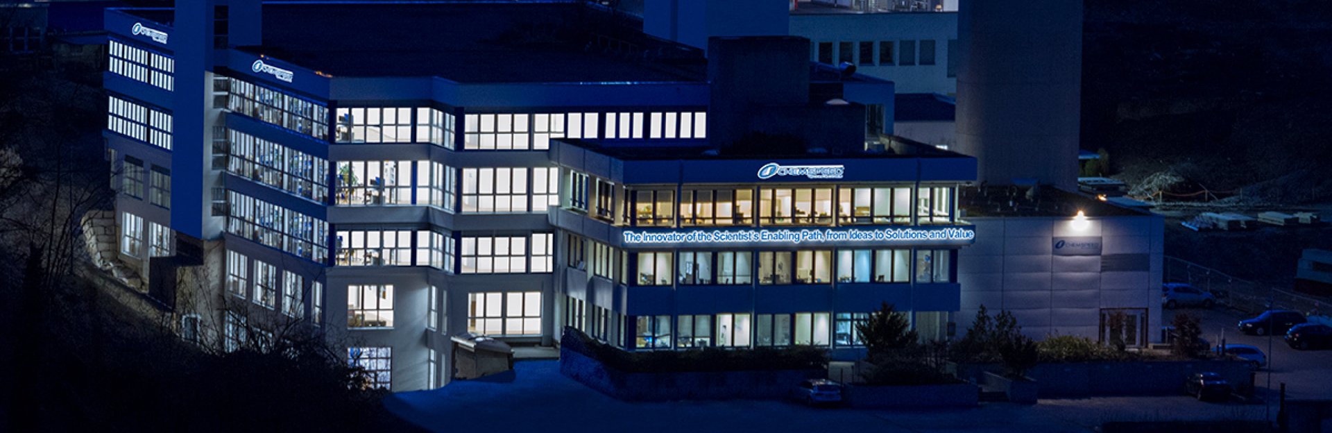 A nighttime drone shot of a large office of Chemspeed with all the lights on in every window