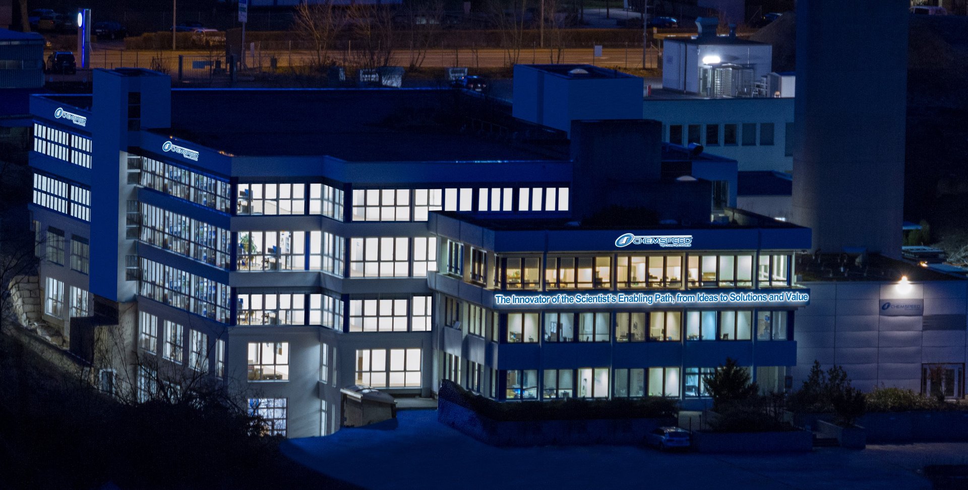 A nighttime shot of Chemspeed's headquarters in fullinsdorf switzerland with all the lights on in the office