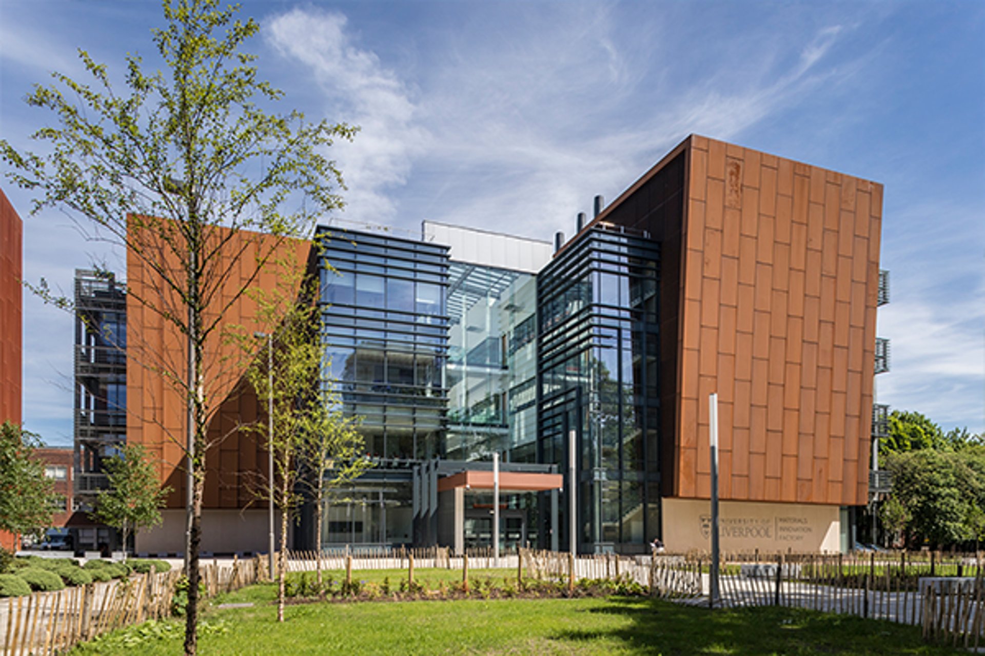 A large modern university MIF building in Liverpool with glass frontage and rusted panels in a grid pattern against a blue sky with light clouds