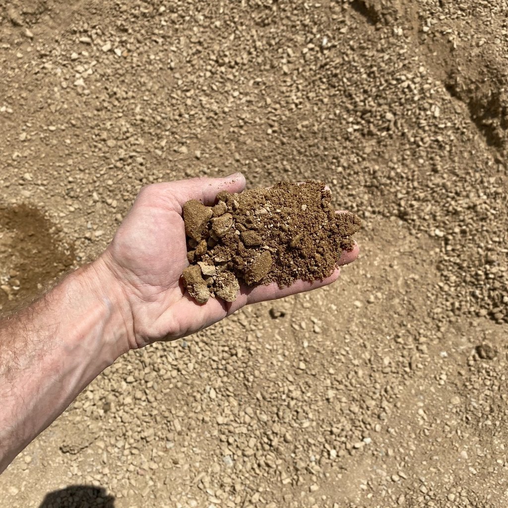 An overhead view of road base compaction gravel with a hand holding the material for scale.