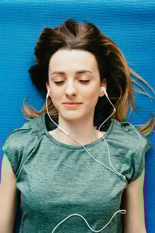 Woman relaxing on a yoga mat with earphones.