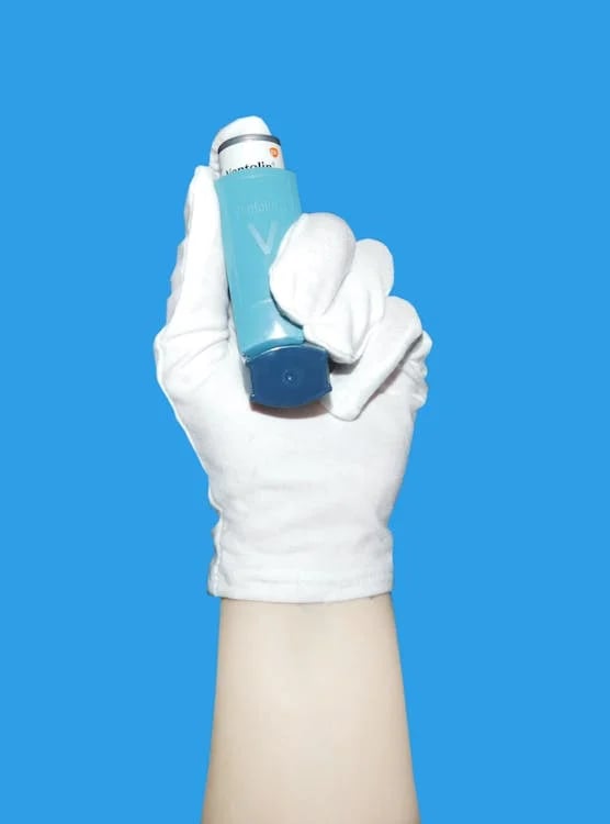 A gloved hand holding an asthma inhaler against a blue background.